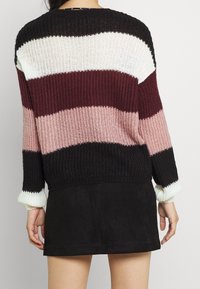 Pruhovaný pletený svetr v černé, vínové, růžové a krémové barvě. Má dlouhé rukávy s žebrovanými manžetami a volný střih.