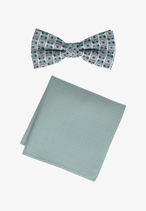 Eine Fliege mit einem bunten geometrischen Muster in Grün und Marineblau auf einem hellen Hintergrund, kombiniert mit einem strukturierten, einfarbigen mintgrünen Taschentuch.