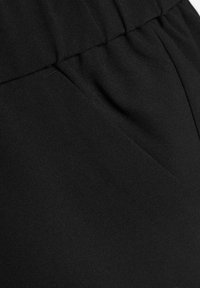 Tessuto nero con una texture liscia, caratterizzato da una cintura elastica e pieghe sottili. Il materiale appare resistente e leggero.