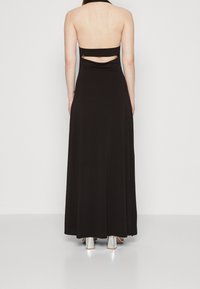 Black halter neck maxi dress with open back, featuring a gathered detail and metallic hardware accent. Smooth, stretchy fabric and full-length design.