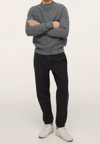 Grauer Kapuzenpullover aus strukturierter Stoff, kombiniert mit schwarzen, schmal zulaufenden Hosen. Weiße Sneaker runden das Outfit ab und sorgen für einen lässigen Look.
