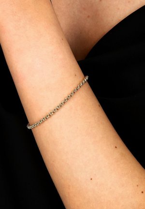 Zarte Goldkette mit kleinen ineinander greifenden Gliedern, die am Unterarm auf einem schwarzen Stoffhintergrund getragen wird.