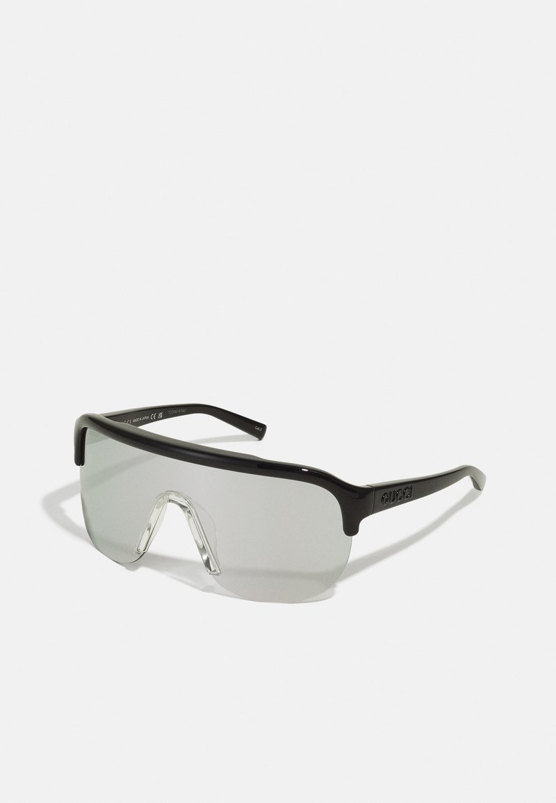 Black sunglasses with a wide, flat lens design. Clear lens with a slight tint, and thick frames. Features logo on the temple.