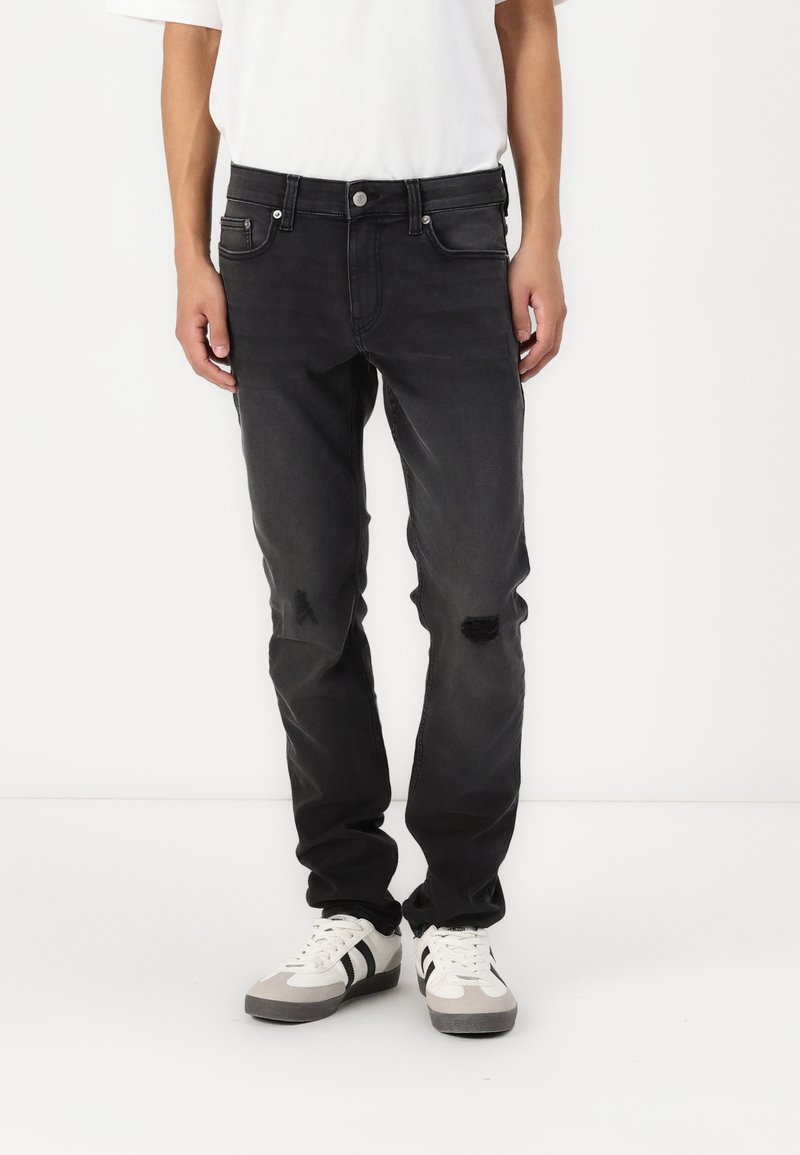 Sorte denimbukser med rett passform, med slitte detaljer og frontlommer. Kombinert med hvite og grå joggesko.