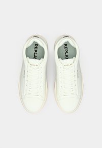 Zapatillas de cuero blanco con un acabado suave, que presentan cordones planos, un cuello acolchado y un logo sutil en el lado y la lengüeta.