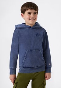 Sudadera con capucha azul hecha de material suave, con un bolsillo frontal y un logo en el pecho, combinada con pantalones cargo verde oliva.