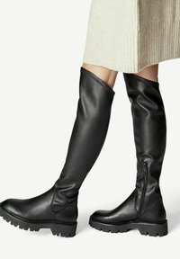 Botas negras hasta la rodilla hechas de cuero texturizado, con cierre de cremallera y suelas de goma gruesa con un diseño de banda de rodadura.