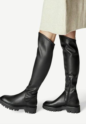 Botas negras hasta la rodilla hechas de cuero texturizado, con cierre de cremallera y suelas de goma gruesa con un diseño de banda de rodadura.