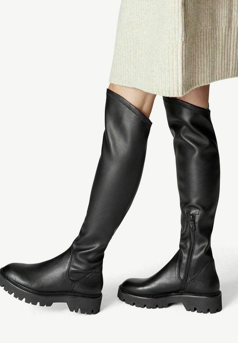 Botas negras hasta la rodilla hechas de cuero texturizado, con cierre de cremallera y suelas de goma gruesa con un diseño de banda de rodadura.