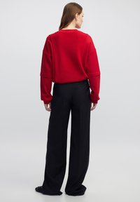 Suéter de punto rojo con hombros caídos y cuello de canalé; combinado con pantalones anchos de tiro alto en negro. Textura de tela suave.