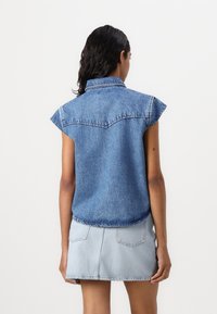 Jeanshemd met een kraag, korte opgerolde mouwen en een losse pasvorm. Kenmerkt zich door achterste schoudernaad details en een vervaagde blauwe kleur. Draagt met een lichtblauwe rok.