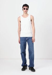 Hvit bomullstopp kombinert med blå denimjeans. Modellen har på seg sorte sneakers og runde solbriller, og viser et avslappet antrekk.