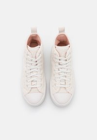 Pár vysokých tenisek s bílou chlupatou texturou, bílými gumovými špičkami, bílými šněrováním a světle růžovým vnitřním podšitím na bílém pozadí.