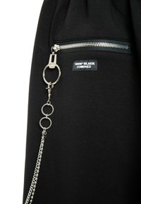 Prenda de algodón negra con un bolsillo con cremalleras, herrajes plateados, un llavero y una cadena decorativa con eslabones circulares adjuntos.
