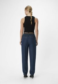 Top negro sin mangas, pantalones sueltos azul oscuro con cintura elástica y zapatos de tacón negros, vistos desde atrás.