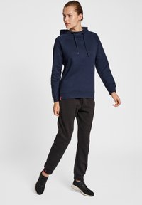 Felpa navy con collo alto e cordini regolabili, abbinata a pantaloni sportivi neri e sneaker nere. Tessuto morbido e vestibilità comoda.