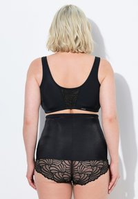 Mustat bralette-laikut leveillä olkaimilla ja pitsi takadetaililla, yhdistettyinä korkeavyötäröisiin mustiin shortseihin, joissa on aaltoileva pitsireuna.
