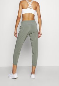 Lichtgrijze sportbroek met een losse pasvorm, elastische tailleband en ritsen bij de enkels. Gecombineerd met een witte sportbeha met bandjes en witte sneakers.