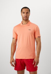 Kortermet polo-skjorte i ferskenfarge med et teksturert mønster, med klassisk krage og svart "BOSS"-logo på brystet.