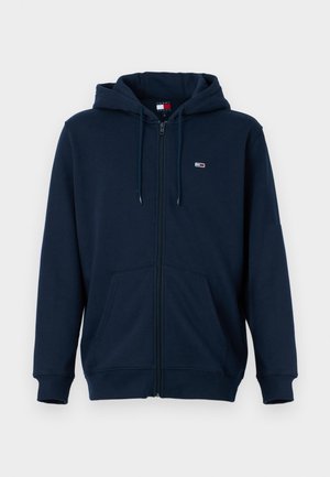 Námornícky modrá mikina na zips z mäkkej tkaniny, s kapucňou na šnúrku, prednými vreckami a malým logom značky na hrudi.