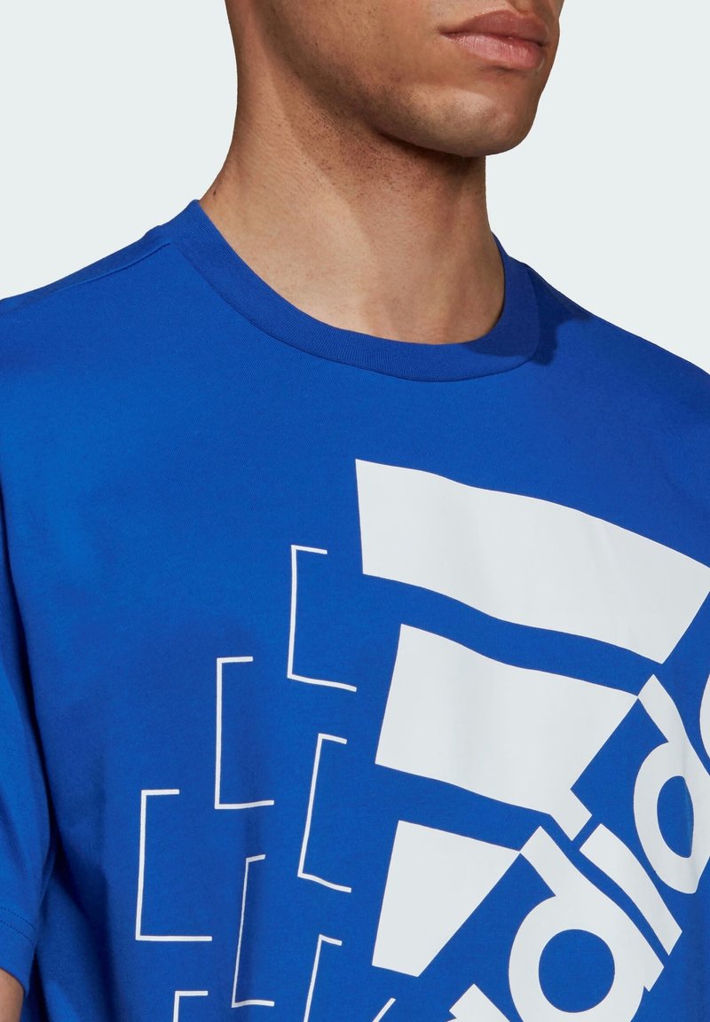 Modrá bavlněná tričko s krátkým rukávem, které na přední straně zdobí velký bílý geometrický grafický design a logo značky.