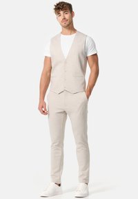 Chaleco beige claro y pantalones ajustados a juego de tela suave, combinados con una camiseta blanca y zapatillas blancas. Vista frontal, diseño casual.