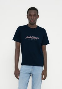 Κοντομάνικο μπλουζάκι σε ναυτικό μπλε χρώμα από βαμβάκι, με κόκκινο και λευκό λογότυπο "Jack & Jones" και την επιγραφή "CREATIVE DEPT" από κάτω.