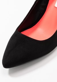 Black suede high-heeled shoe with a pointed toe and a vibrant coral insole. The design features a smooth texture and a sleek silhouette.