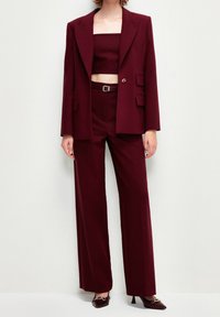 Burgundy skräddarsydd kostym med en dubbelknäppt kavaj, vida byxor och en figurnära crop top, kompletterad med eleganta högklackade skor.