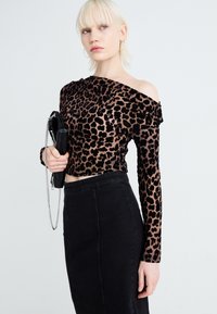 Leopárdmintás, vállra hulló, áttetsző anyagból készült felső, amelyet egy magas derékú fekete farmer szoknyával párosítanak. Fekete clutch táska láncos pánttal.