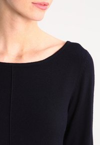 Maglione lavorato a maglia blu navy con scollatura arrotondata, texture liscia e dettagli di cucitura sottili sulle maniche e sul torso.