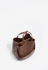 Bolso tote de cuero marrón con doble asa, cremallera dorada y una correa para el hombro que presenta "BIMBA Y LOLA" en un color claro. Compartimentos interiores visibles.