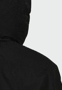 Giacca nera impermeabile con superficie testurizzata e gocce d'acqua. Il cappuccio è visibile, mostrando una finitura opaca e un design senza cuciture.