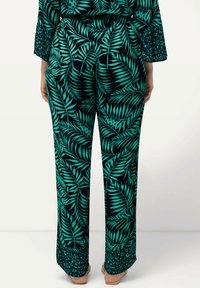 Svarta byxor med stora gröna lövmönster, vida ben och en dekorativ leopardmönstrad accent vid fållen. Tillverkade av mjukt, slätt tyg.