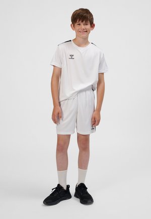 Weißes Sporttrikot und Shorts mit schwarzen Akzenten und Logo, kombiniert mit schwarzen Sportschuhen und weißen Socken. Der Stoff wirkt leicht.