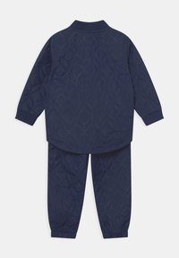 Granatowy pikowany zestaw kurtka i spodnie z przeszyciami w kształcie diamentów oraz elastycznymi mankietami, pokazany od tyłu.