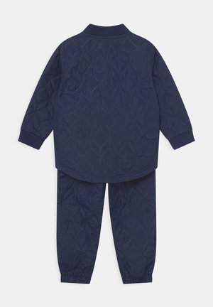 Marineblauw gewatteerd jack en broekset met ruitvormige stiknaden en elastische manchetten, vanaf de achterkant getoond.