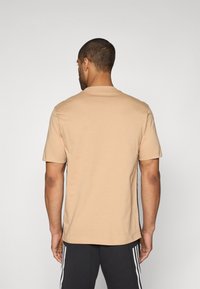Beige bomulds t-shirt med korte ærmer og rund halsudskæring, vist fra ryggen. Har en afslappet pasform og glat tekstur.