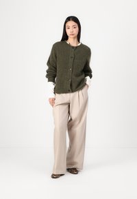 Cardigan verde măsliniu cu guler rotund, închidere cu nasturi și tricot texturat. Asortat cu pantaloni largi bej și pantofi cu imprimeu leopard.