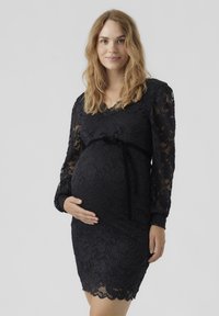 Melna mežģīņu grūtnieču kleita ar garām piedurknēm, V veida kakla izgriezumu, pieguļošu siluetu un noņemamu melnu samtu jostu, kas izceļ vidukli.