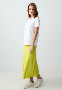 WeißesT-Shirt mit kurzen Ärmeln, kombiniert mit einem knielangen, leuchtend limettengrünen Rock und weißen Sneakers mit strukturierten Sohlen und Schnürsenkeln.