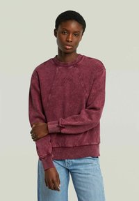 Felpa bordeaux con scollo rotondo, maniche a raglan e polsini a costine. Presenta un ricamo testurizzato del logo e una vestibilità rilassata.