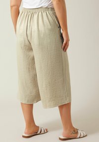 Beige, lichte, cropped broeken van een gestructureerde stof, met een elastische tailleband en zijzakken. Gedragen met witte sandalen met bandjes.