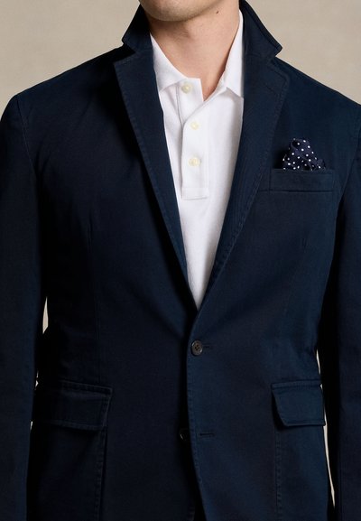 Blazer blu navy in cotone con colletto a revers, chiusura con un unico bottone e tasca sul petto a sinistra contenente un fazzoletto a pois.