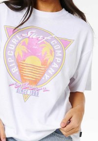 Hvid kortærmet t-shirt med et farverigt grafisk design af en solnedgang med palmer og teksten "RIP CURL Surf Company" i forskellige farver.