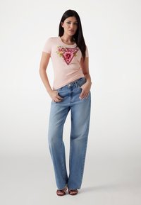 Lyserød t-shirt med blomstertriangel grafik; parret med brede lyseblå jeans. Sættet har en afslappet pasform og en uformel stil.