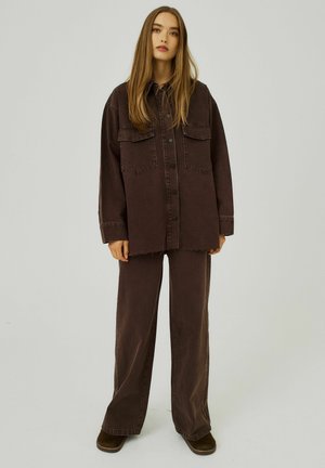 Bruine denim overhemd met twee borstzakken, knoopsluiting en rafelige zoom, gecombineerd met bijpassende wijdere broek in een vergelijkbare tint. Zachte textuur.