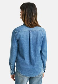Denimskjorte, lyseblå, langermet med knappmansjetter, buet nederkant og detalj med legg bak. Standard krageform, avslappet passform.