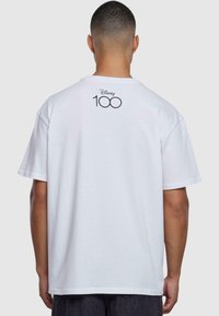 Hvit bomulls t-skjorte med "Disney 100"-logo trykt på baksiden. Kort erm med avslappet passform og rund hals.