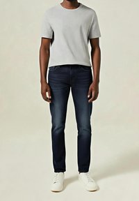 Camiseta de manga corta de color gris claro combinada con jeans azul oscuro y zapatillas blancas. El conjunto tiene un ajuste casual y texturas suaves.